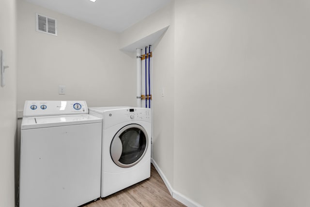 laundry room with independent washer and dryer and light hardwood / wood-style flooring