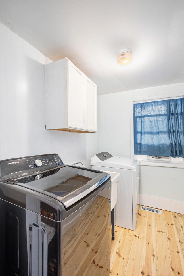 laundry area featuring washing machine and dryer, light hardwood / wood-style flooring, and cabinets