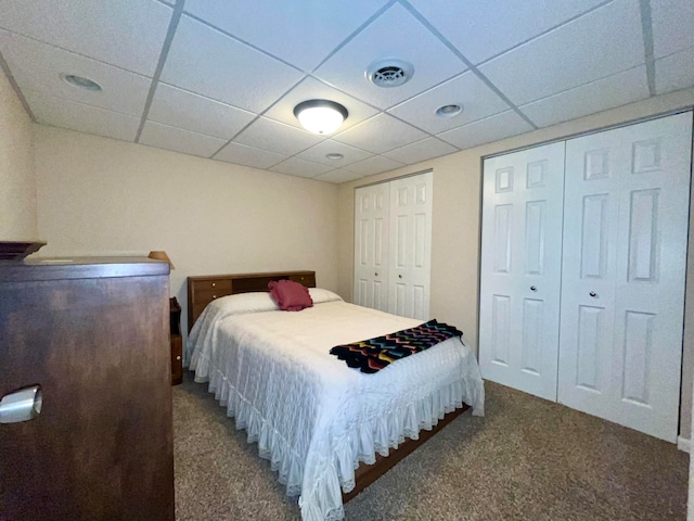 bedroom with carpet flooring, a paneled ceiling, and two closets