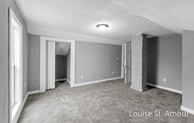 unfurnished bedroom featuring carpet flooring, decorative columns, a textured ceiling, lofted ceiling, and a closet