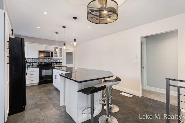 kitchen featuring a breakfast bar, black appliances, decorative light fixtures, a kitchen island, and white cabinetry