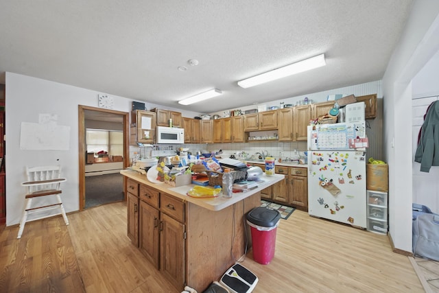 kitchen featuring backsplash, a textured ceiling, white appliances, light hardwood / wood-style flooring, and a center island