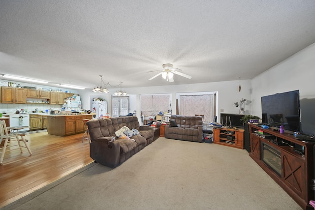 carpeted living room featuring ceiling fan with notable chandelier and a textured ceiling