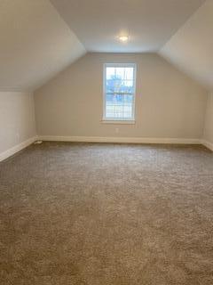 bonus room with lofted ceiling and dark colored carpet