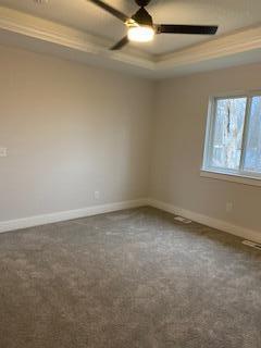 spare room featuring dark colored carpet, ceiling fan, ornamental molding, and a tray ceiling