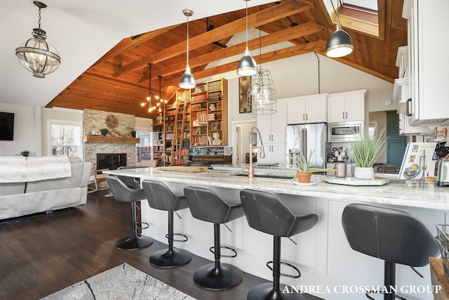 kitchen with white cabinetry, stainless steel appliances, light stone counters, beamed ceiling, and dark hardwood / wood-style floors