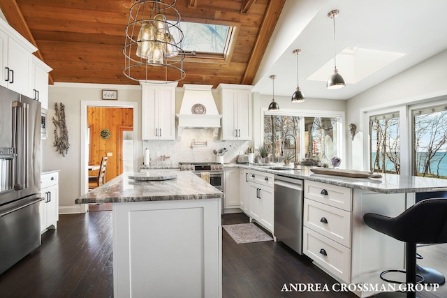 kitchen featuring pendant lighting, lofted ceiling with skylight, premium appliances, a kitchen island, and light stone counters