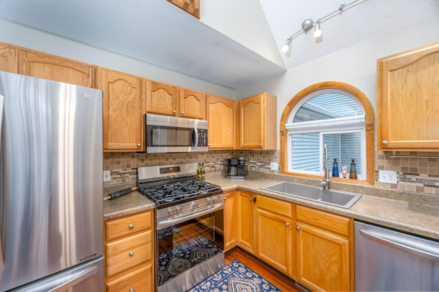 kitchen with lofted ceiling, sink, hardwood / wood-style flooring, decorative backsplash, and appliances with stainless steel finishes