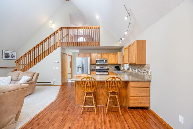 kitchen with baseboard heating, high vaulted ceiling, kitchen peninsula, light hardwood / wood-style floors, and appliances with stainless steel finishes