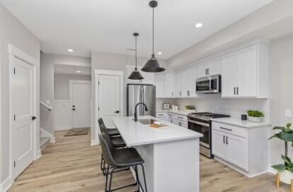 kitchen featuring appliances with stainless steel finishes, light hardwood / wood-style floors, white cabinetry, and an island with sink