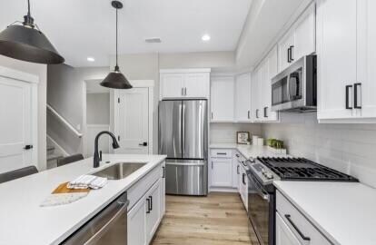 kitchen featuring white cabinetry, pendant lighting, light hardwood / wood-style floors, and appliances with stainless steel finishes