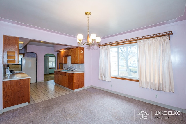 kitchen featuring sink, a chandelier, hanging light fixtures, fridge, and light colored carpet