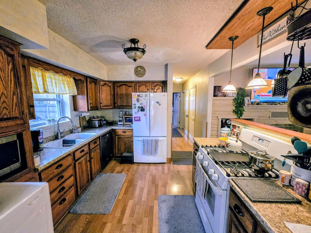 kitchen with gas stove, sink, decorative light fixtures, light hardwood / wood-style flooring, and white fridge