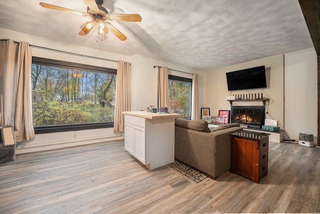 living room featuring ceiling fan, plenty of natural light, light hardwood / wood-style floors, and a textured ceiling