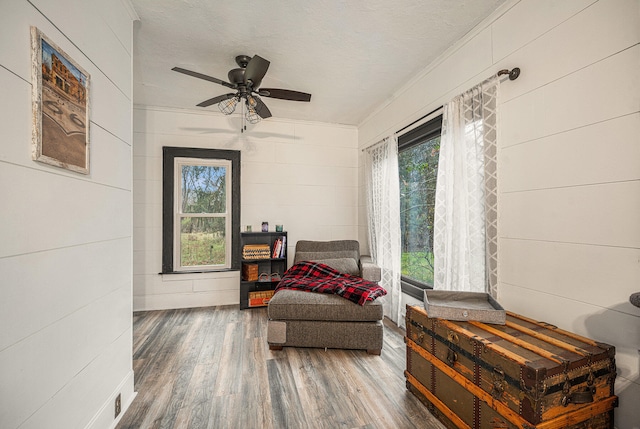 living area with ceiling fan, dark hardwood / wood-style flooring, ornamental molding, and a textured ceiling