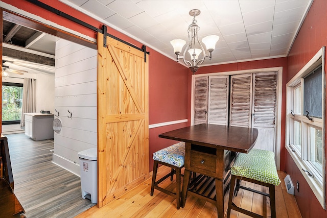 dining room with wooden walls, crown molding, a barn door, hardwood / wood-style flooring, and a chandelier