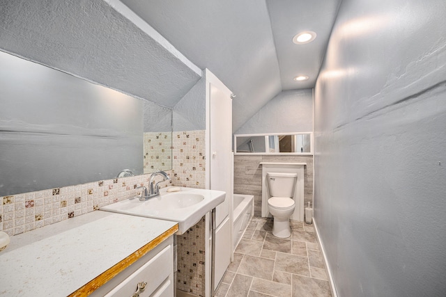 bathroom featuring vanity, a bath, vaulted ceiling, toilet, and tile walls