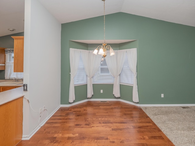 unfurnished dining area featuring lofted ceiling, hardwood / wood-style flooring, a notable chandelier, and sink