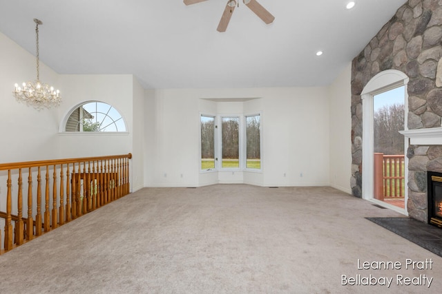 unfurnished living room featuring carpet, ceiling fan with notable chandelier, and a stone fireplace