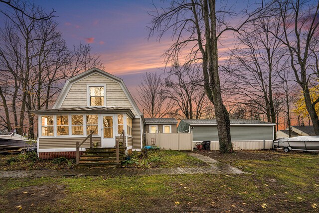 back house at dusk with a lawn and a sunroom