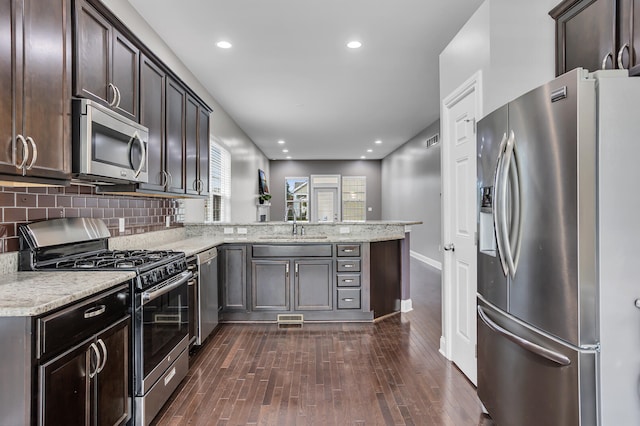 kitchen featuring stainless steel appliances, dark hardwood / wood-style flooring, backsplash, kitchen peninsula, and dark brown cabinets