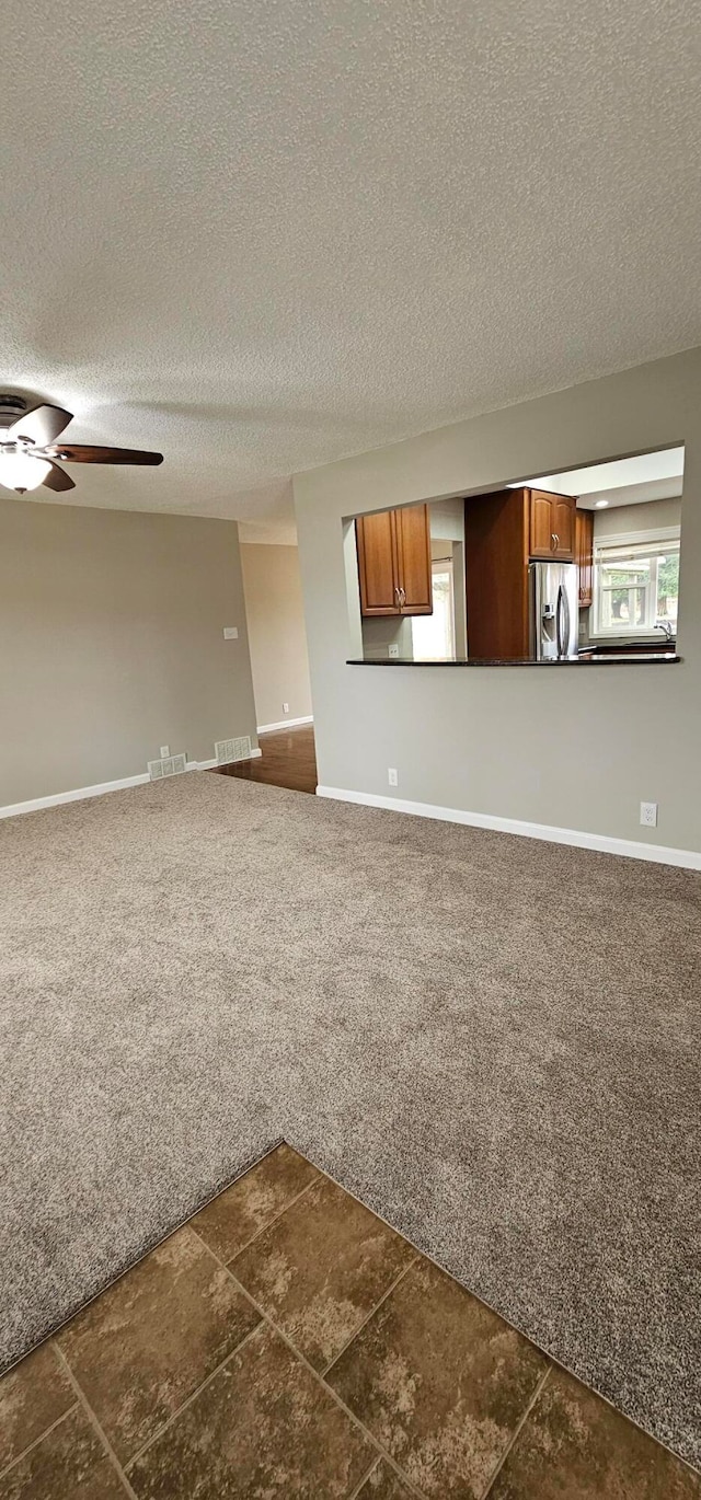 unfurnished living room featuring ceiling fan, dark carpet, and a textured ceiling