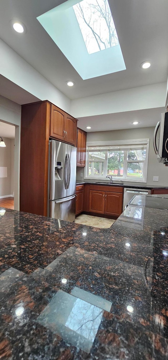 kitchen featuring a skylight, sink, dark stone countertops, and appliances with stainless steel finishes