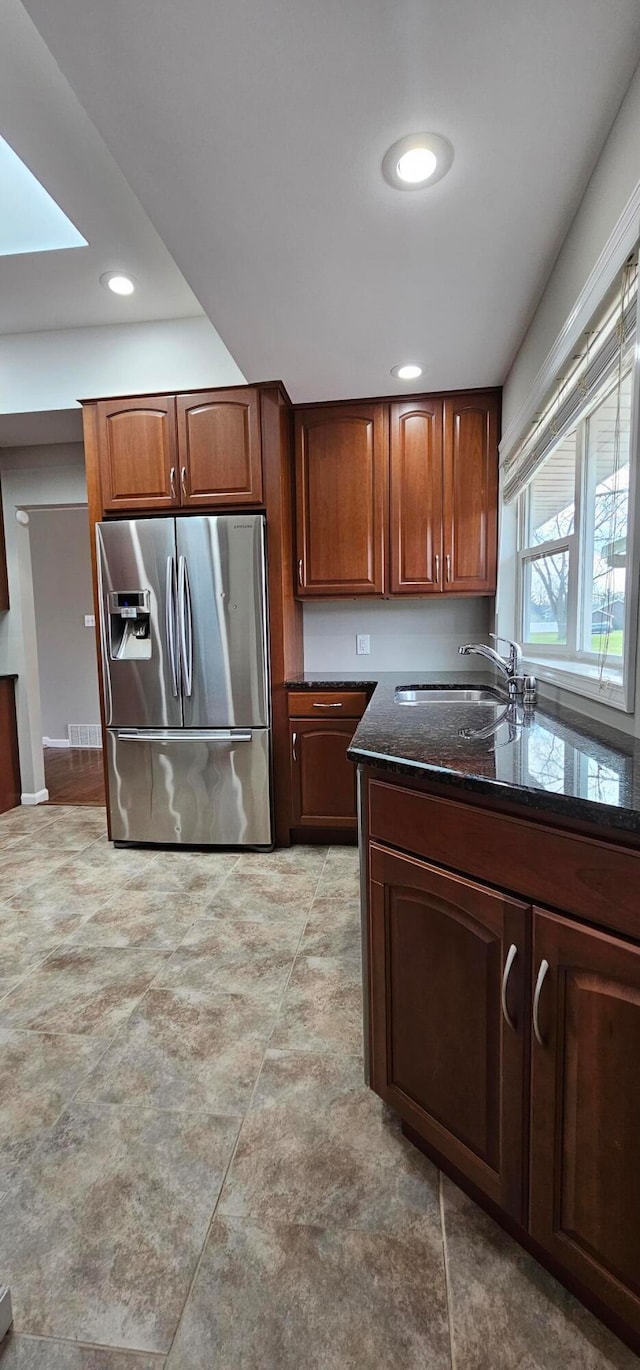 kitchen featuring stainless steel fridge with ice dispenser, a skylight, dark stone counters, and sink