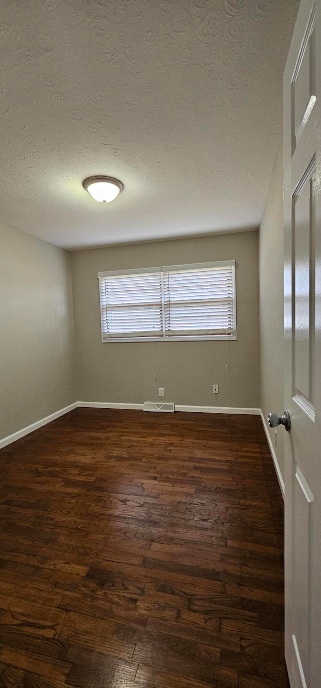 empty room with dark hardwood / wood-style flooring and a textured ceiling