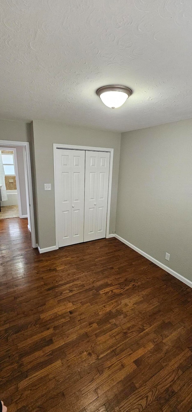 unfurnished bedroom featuring a textured ceiling, dark hardwood / wood-style flooring, and a closet