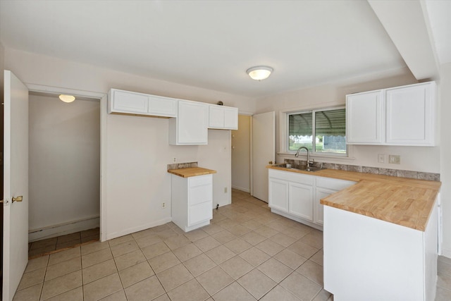 kitchen featuring wood counters, light tile patterned floors, white cabinets, and sink