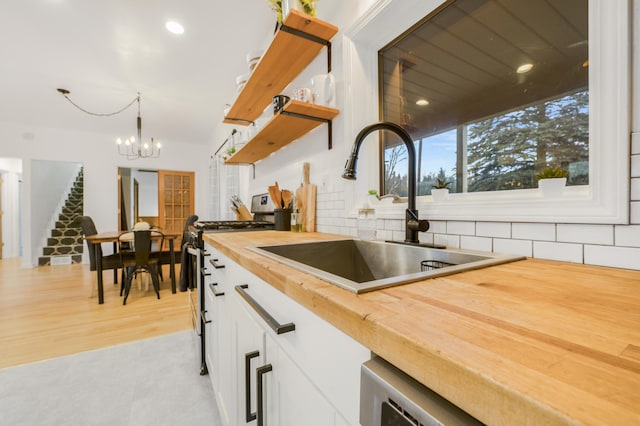 kitchen with pendant lighting, white cabinets, stainless steel range with gas cooktop, sink, and butcher block countertops