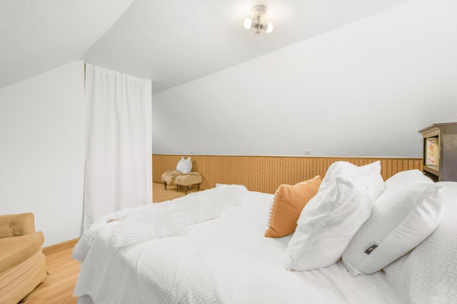 bedroom featuring light hardwood / wood-style floors, wooden walls, and vaulted ceiling