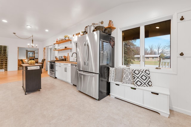 kitchen with stainless steel appliances, a kitchen island, butcher block countertops, a chandelier, and white cabinets