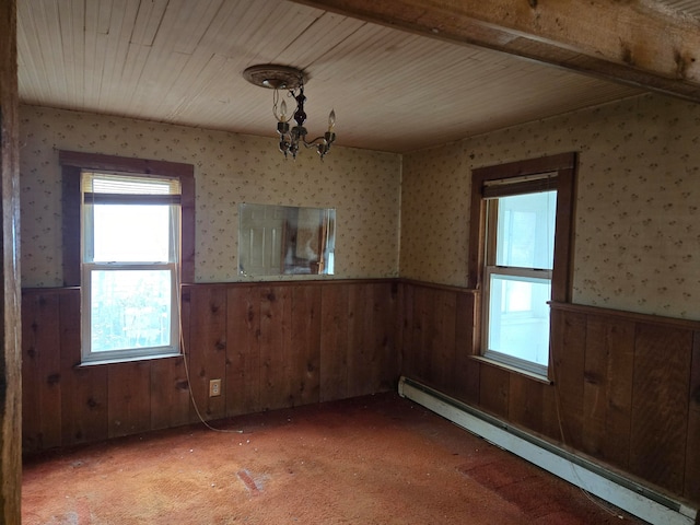 spare room with a notable chandelier, wood walls, light colored carpet, and a baseboard heating unit