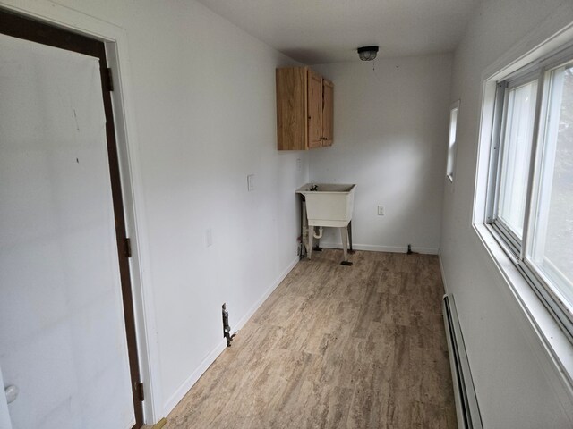 laundry room featuring cabinets, sink, a baseboard radiator, and light hardwood / wood-style flooring