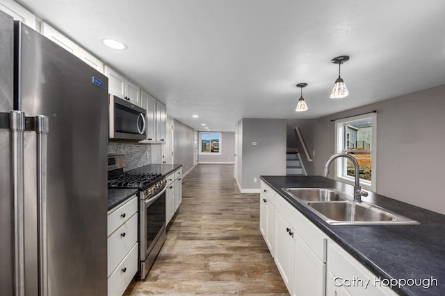 kitchen with white cabinetry, sink, hanging light fixtures, stainless steel appliances, and light wood-type flooring