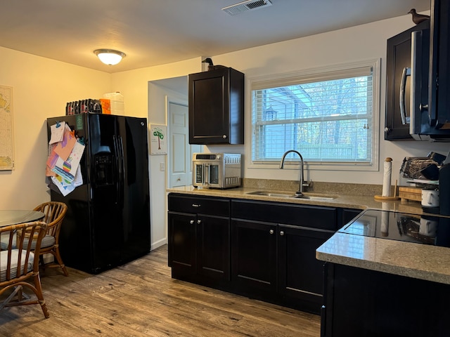 kitchen with black fridge with ice dispenser, light wood-type flooring, and sink