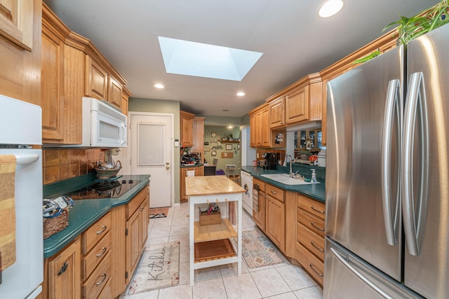 kitchen featuring white appliances, sink, light tile patterned floors, and a skylight