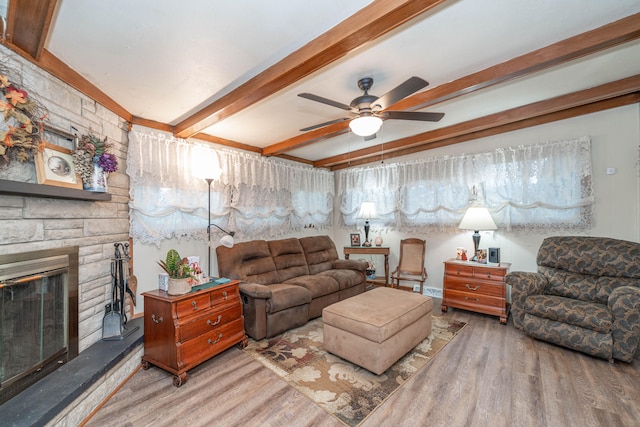 living room with a stone fireplace, ceiling fan, beamed ceiling, and hardwood / wood-style flooring