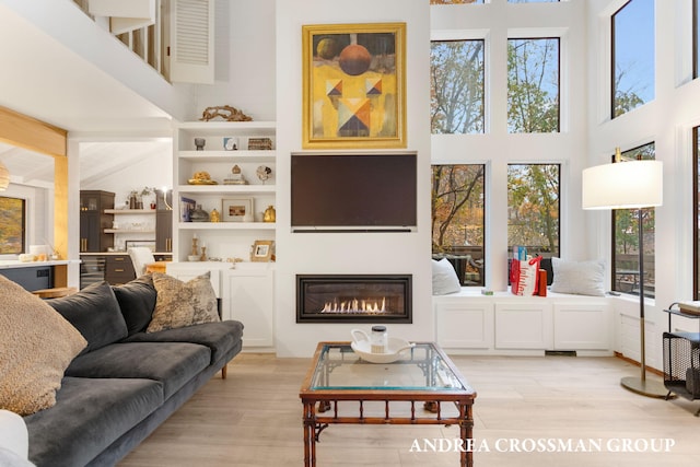 living room featuring a towering ceiling, a healthy amount of sunlight, and light wood-type flooring