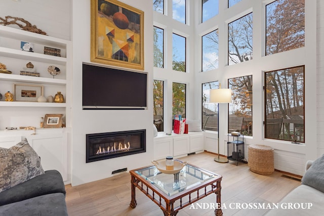 living room featuring a high ceiling, plenty of natural light, light hardwood / wood-style floors, and built in features