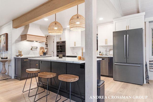 kitchen with premium range hood, white cabinets, appliances with stainless steel finishes, decorative light fixtures, and a breakfast bar area