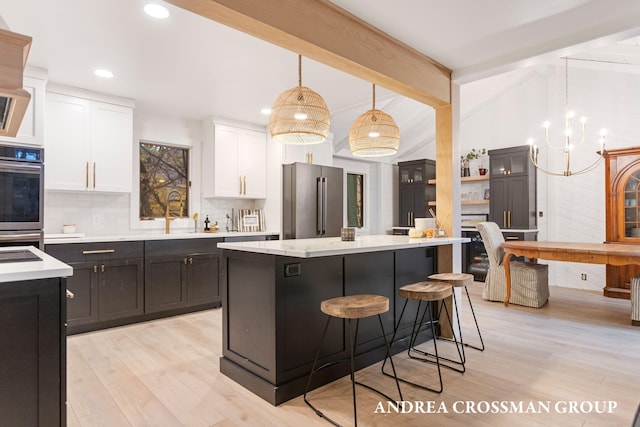 kitchen with a center island, white cabinets, hanging light fixtures, light wood-type flooring, and appliances with stainless steel finishes