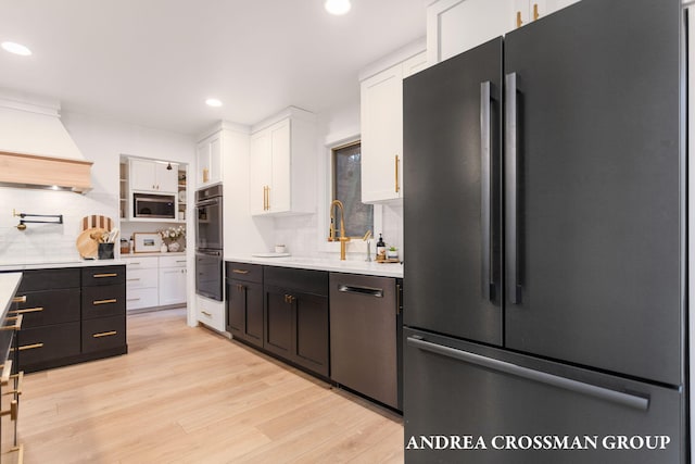 kitchen with light wood-type flooring, backsplash, custom range hood, stainless steel appliances, and white cabinetry