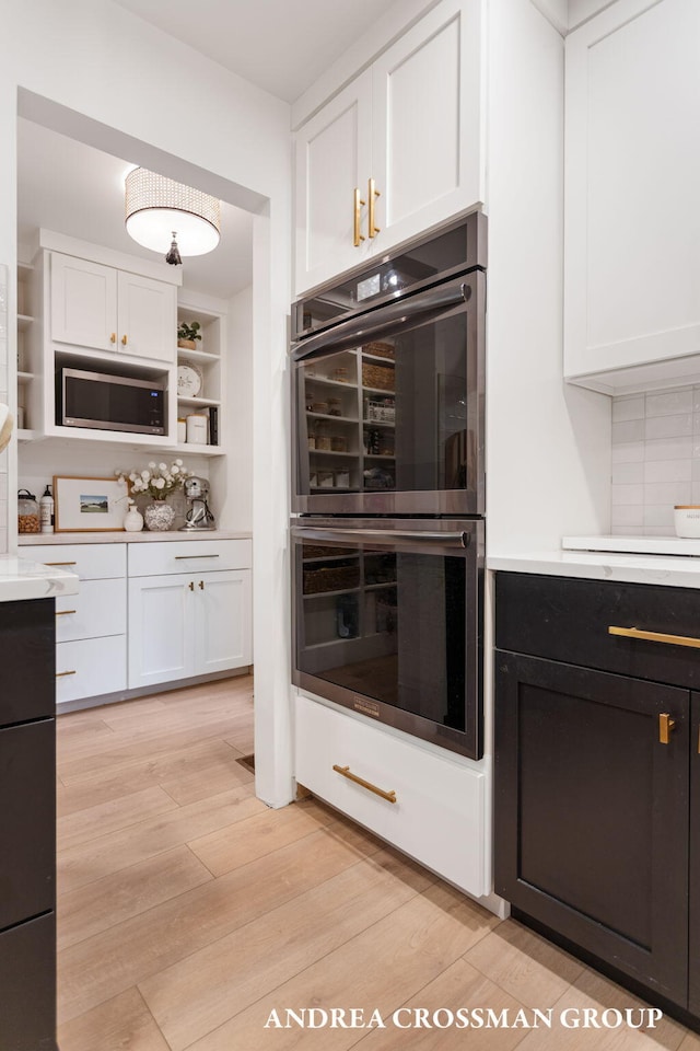 kitchen with white cabinets, appliances with stainless steel finishes, light wood-type flooring, and backsplash