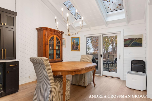 dining space featuring vaulted ceiling with skylight, wood walls, an inviting chandelier, and light hardwood / wood-style flooring