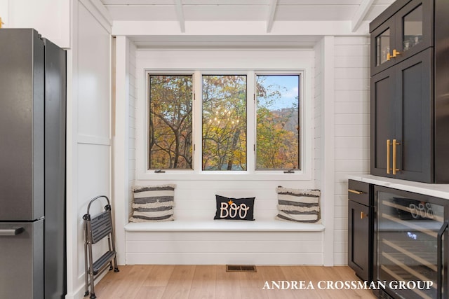 sitting room featuring wine cooler, beamed ceiling, and light wood-type flooring