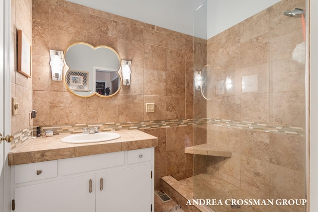 bathroom with a tile shower, decorative backsplash, vanity, and tile walls