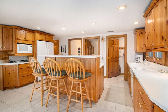 kitchen featuring a kitchen breakfast bar, tasteful backsplash, white appliances, sink, and light tile patterned floors